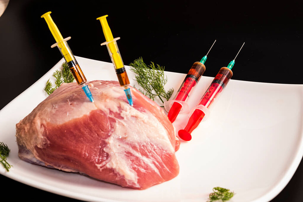 Inyección de una jeringa en carne cruda sobre un fondo oscuro.Ilustración conceptual de hormonas y antibióticos en la producción de alimentos. - Foto, imagen