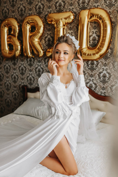 Beautiful young bride in white peignoir lying on bed in hotel bedroom. Final preparations for the wedding. The bride is waiting for the groom. Morning, bride. - Valokuva, kuva