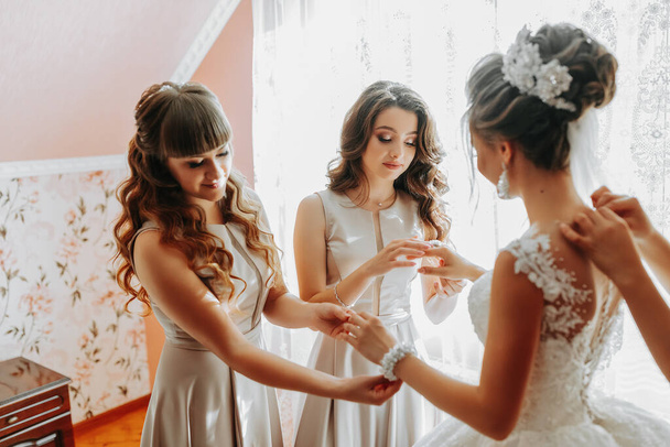 Brautfreundin bereitet die Braut auf ihren Hochzeitstag vor. Die Freundin der Braut hilft, das Brautkleid vor der Zeremonie zu sichern. - Foto, Bild