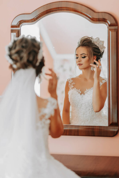 The bride in a beautiful dress looks in the mirror, the last preparations. Wedding. wedding bouquet Morning of the bride. A happy bride is waiting for the groom. - Zdjęcie, obraz