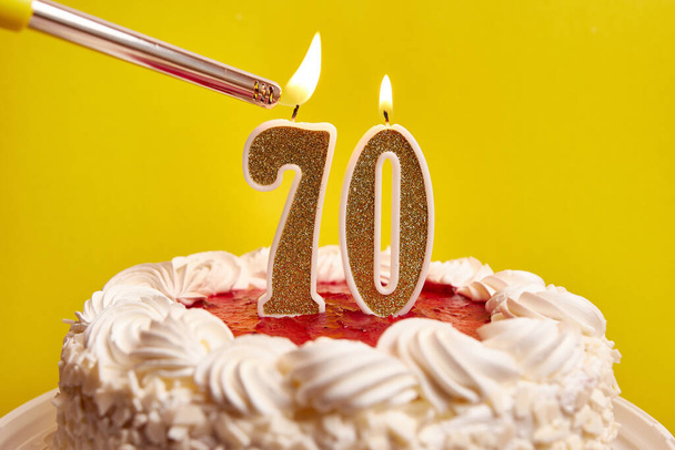 A candle in the form of the number 70, stuck in a festive cake, is lit. Celebrating a birthday or a landmark event. The climax of the celebration. - Foto, Imagem