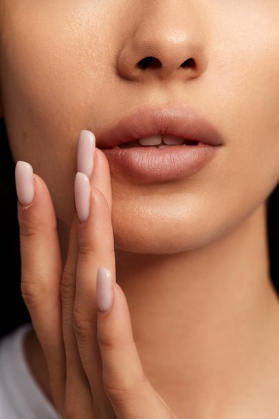 Crop unrecognizable female with smooth skin touching lips with fingers while applying herpes balm during skincare treatment - Foto, imagen