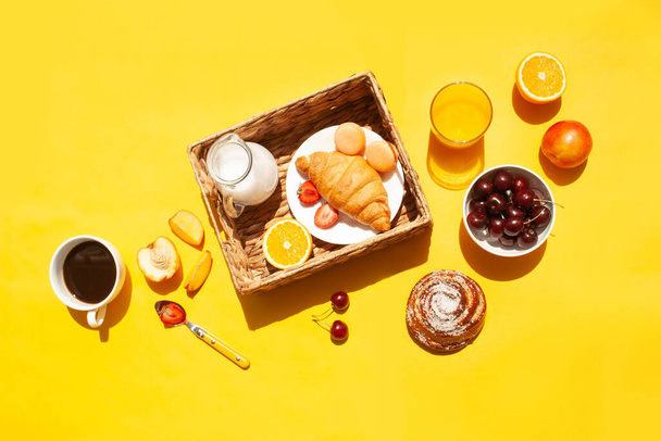 Breakfast with a cup of coffee, fruits and croissants on a yellow background top view. Flat lay style - Foto, afbeelding