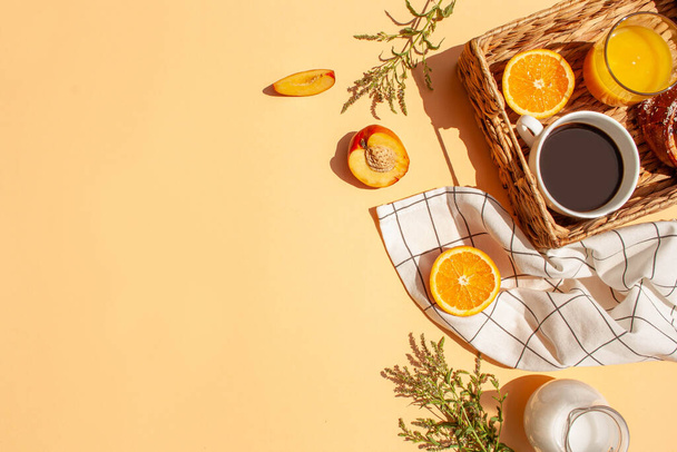 Desayuno soleado por la mañana. Café, zumo de naranja, frutas frescas en una canasta de mimbre sobre un fondo de melocotón. Estilo de laico plano - Foto, imagen
