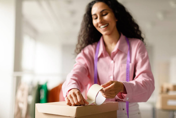 Fashion Stylist Woman Packing Box With Clothing Order Preparing Fashionable Clothes For Client Standing In Trendy Showroom. Small Business And Delivery. Selective Focus On Adhesive Tape - Fotoğraf, Görsel