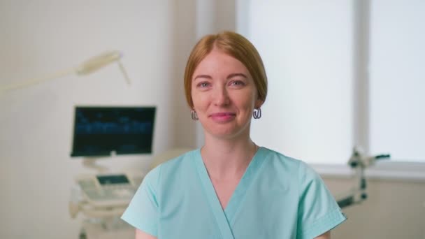 hymyilevä gynekologi lääkäri gynekologinen toimisto lähellä ultraääni ja gynekologinen tuoli odottaa potilaita - Materiaali, video
