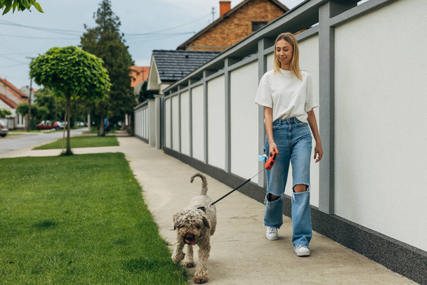 Pretty young woman walking the dog in the neighborhood. - Фото, изображение