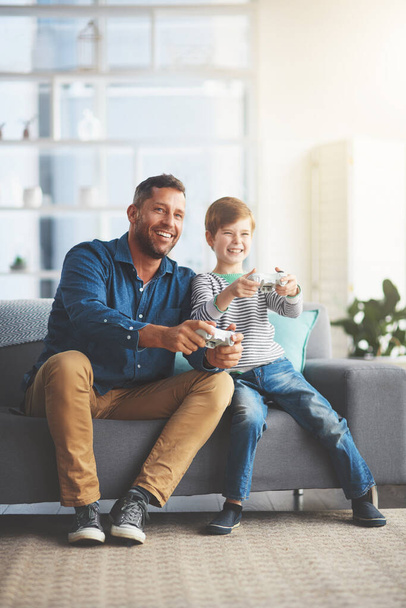 Oh its on now. a cheerful little boy and his father playing video games together on the television while being seated on the sofa at home during the day - Foto, Imagen