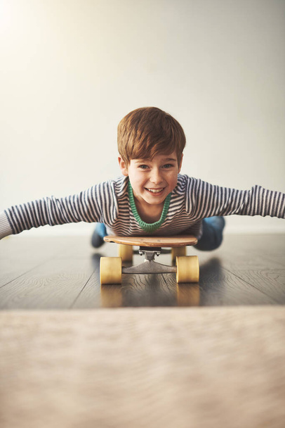 I dont need to stand on a skateboard to have fun. Portrait of a cheerful little boy lying down on a skateboard at home during the day - Photo, image