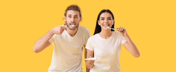 Young couple brushing teeth on yellow background - Foto, Imagem