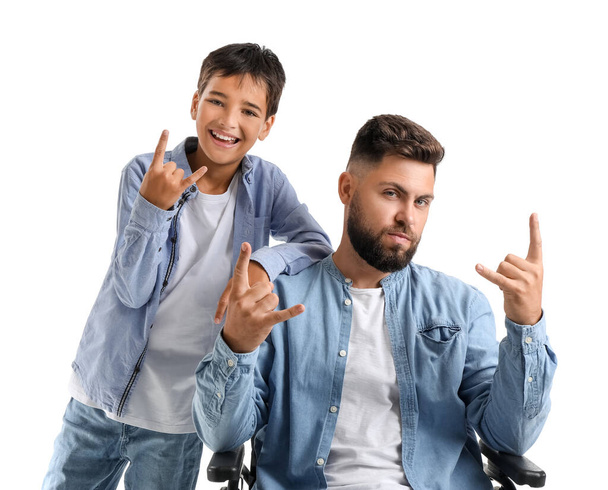 Kleiner Junge und sein Vater im Rollstuhl zeigen "Teufelshörner" -Geste auf weißem Hintergrund - Foto, Bild