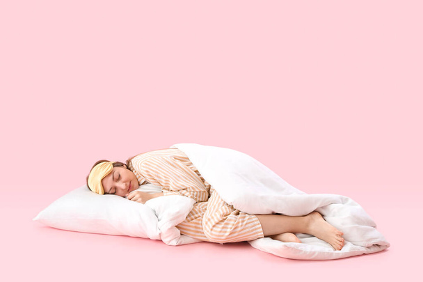 Молодая женщина в пижаме с одеялом и подушкой спит на розовом фоне - Фото, изображение