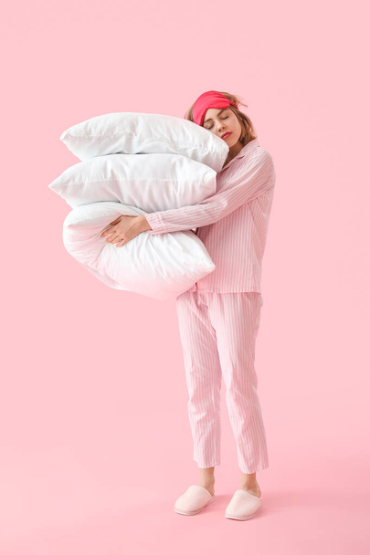 Schläfrige junge Frau im Schlafanzug mit Kissen auf rosa Hintergrund - Foto, Bild