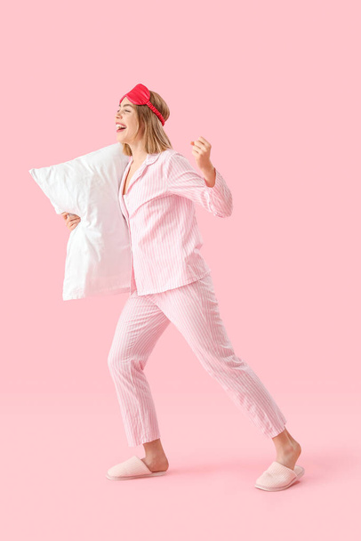 Ευτυχισμένη νεαρή γυναίκα με πιτζάμες με μαξιλάρι σε ροζ φόντο - Φωτογραφία, εικόνα
