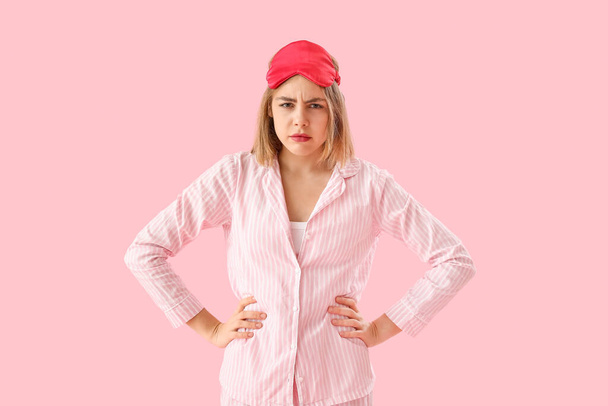Mujer joven trastornada en pijama sobre fondo rosa - Foto, Imagen