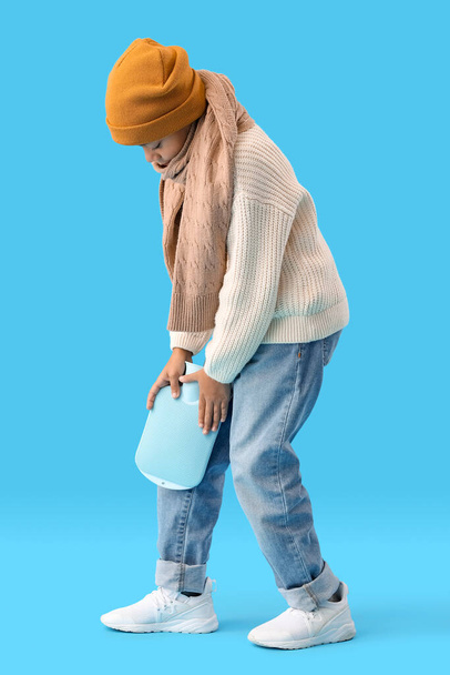 Больной афроамериканец греет колено бутылкой горячей воды на синем фоне. - Фото, изображение