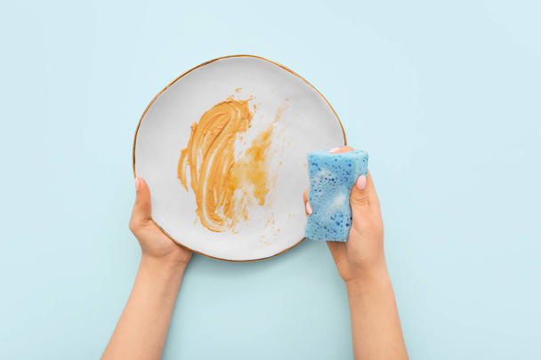 Жіночі руки миють брудну тарілку з губкою на синьому фоні
 - Фото, зображення