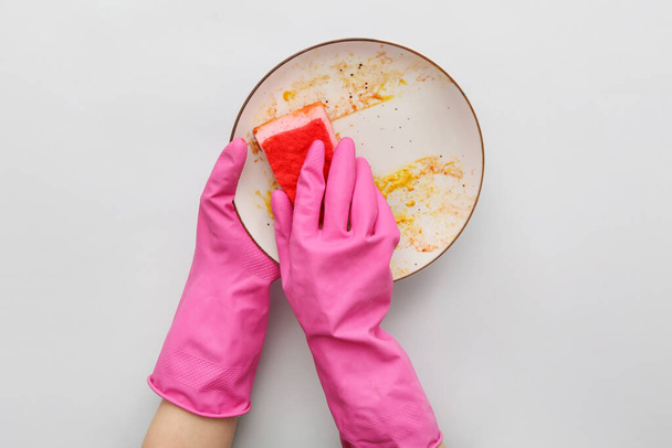 Mãos femininas em luvas de borracha lavar prato sujo com esponja no fundo cinza - Foto, Imagem