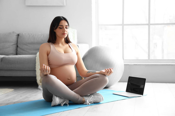 Urheilullinen nuori raskaana oleva nainen meditoi kotona - Valokuva, kuva