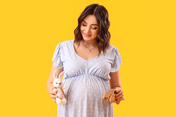 Young pregnant woman with baby toys on yellow background - Foto, Bild