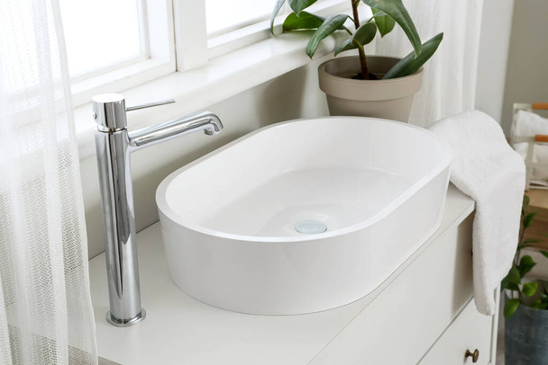 Vaschetta lavabo, rubinetto e pianta d'appartamento su cassettiera vicino alla finestra - Foto, immagini