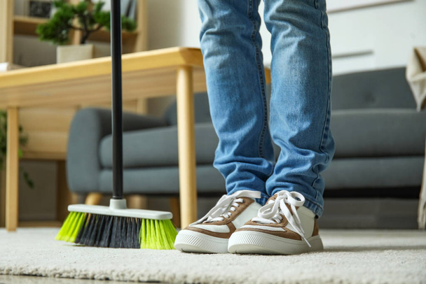 Young man sweeping carpet with broom at home, closeup - Foto, Bild