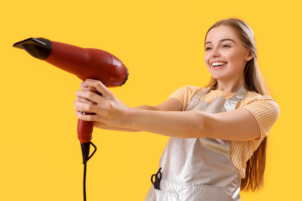 Female hairdresser with dryer on yellow background - Photo, Image