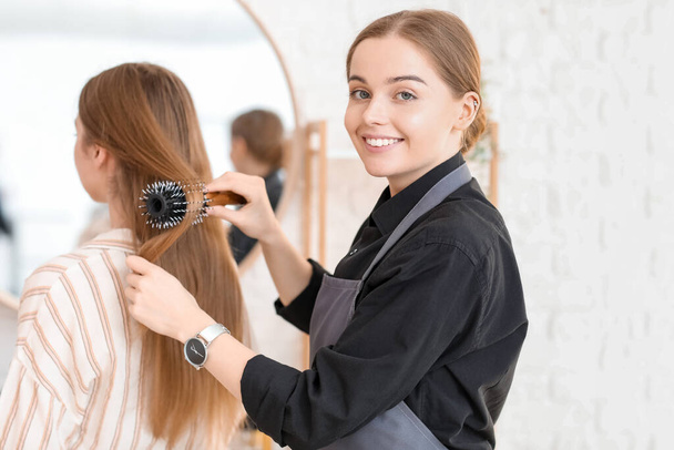 Female hairdresser brushing young woman's hair in beauty salon - Foto, Imagen