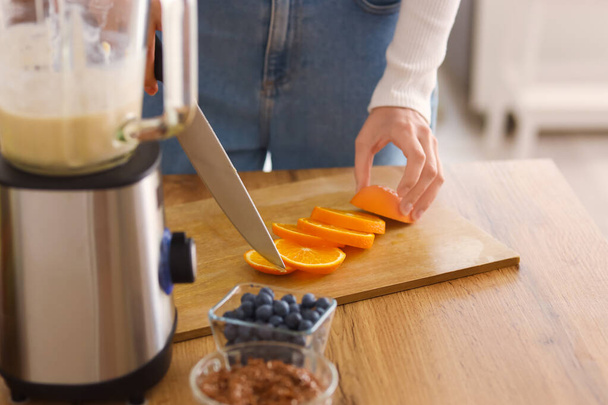 Young woman cutting orange in kitchen, closeup - Foto, Imagen