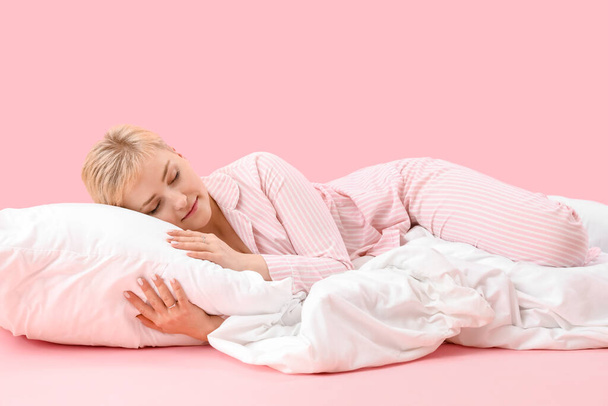 Giovane donna con cuscino e morbida coperta dormire su sfondo rosa - Foto, immagini