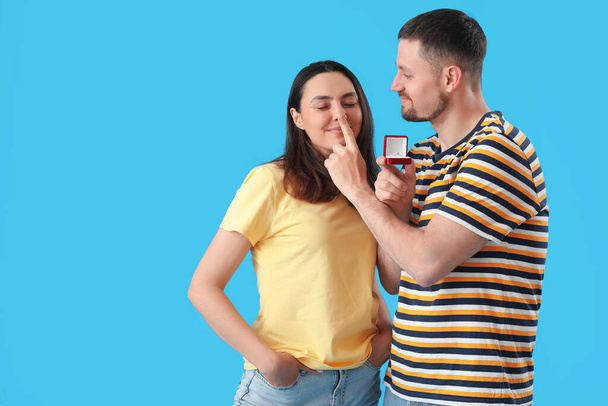 Feliz joven pareja con anillo de compromiso sobre fondo azul - Foto, imagen