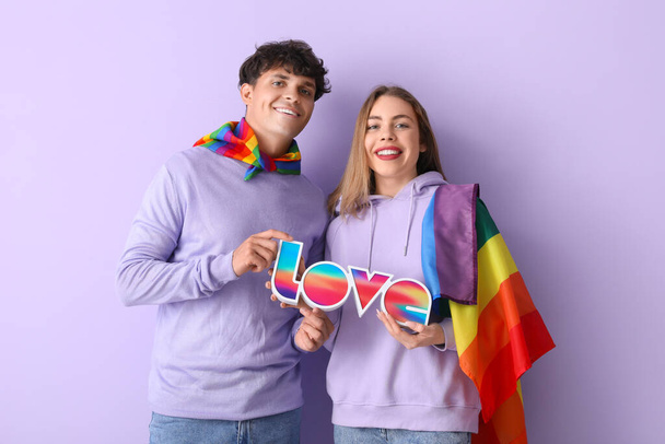Молода пара з ЛГБТ - прапором і словом "ЛЮБОВ" на фоні лілаку - Фото, зображення