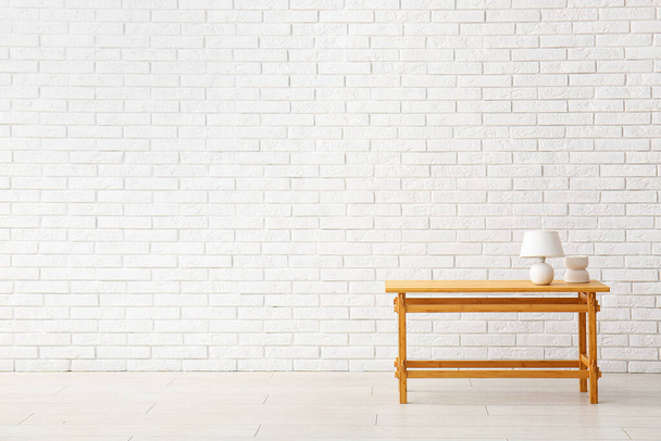 Wooden table with lamp and decorative figure near white brick wall - Foto, afbeelding