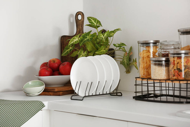 Lemeztartó, alma, szobanövény és üvegek különböző ételekkel a fehér konyhapulton, közelkép - Fotó, kép