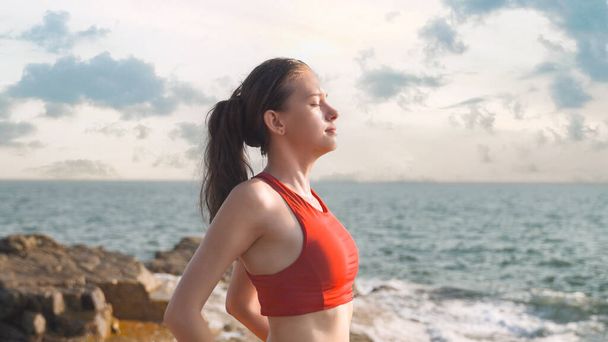 mujer joven en ropa deportiva respira profundamente el aire del mar después del yoga. Foto de alta calidad - Foto, Imagen
