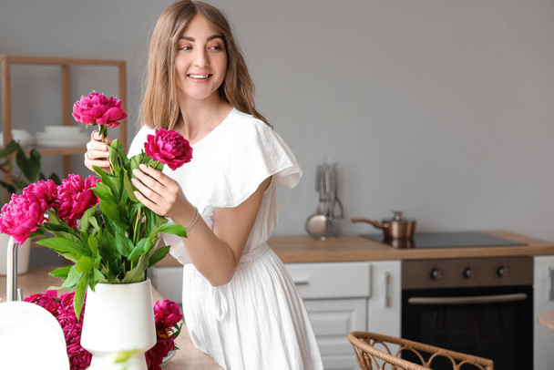 Gyönyörű fiatal nő csokor bazsarózsa virágok a konyhában - Fotó, kép