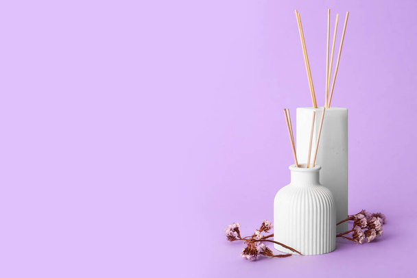 Bottles of reed diffuser and flowers on purple background - Fotoğraf, Görsel
