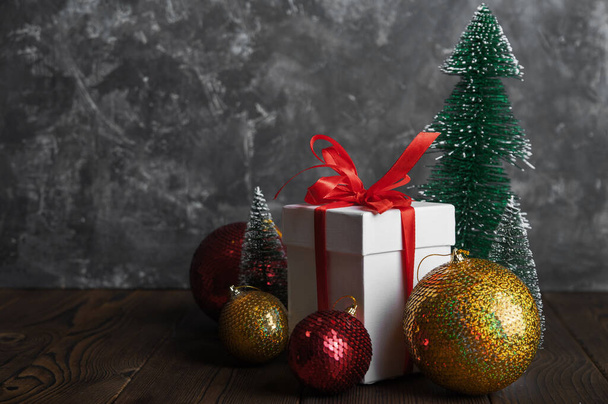 Vánoční přání na tmavém pozadí. Krabice s dárkem, vánoční koule, stromy a kopírovací prostor. - Fotografie, Obrázek