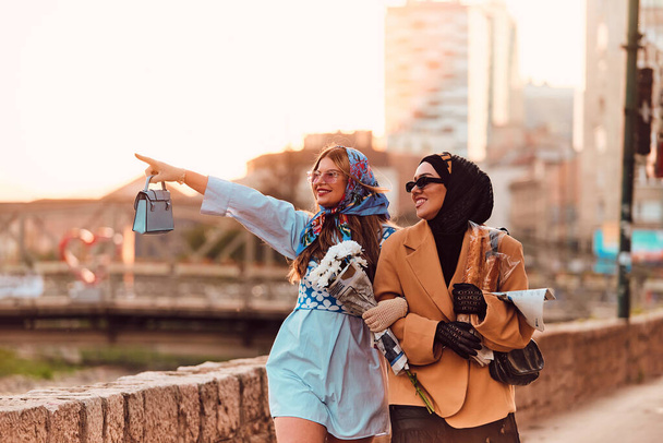 Pari nainen toinen yllään hijabi ja moderni mutta perinteinen mekko, ja toinen sininen mekko ja huivi, kävely yhdessä läpi kaupungin auringonlaskun aikaan. Yksi kuljettaa kimppu ja leipää, kun taas - Valokuva, kuva