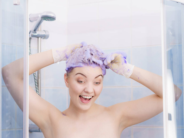 Saçına boya şampuanı süren bir kadın. Mor çamaşır ürünleri olan bir kadın. Evde sarı tonlama. - Fotoğraf, Görsel
