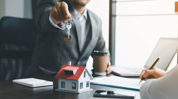 Home sales and home insurance concept. Estate agent giving house keys to woman and asked the customer to sign the documents to make the contract legally. - Foto, immagini
