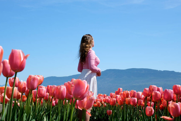 meisje in wit rok loopt door een veld tulpen dansen draaiende run touch bloemen met haar handen rechttrekken haar op blauwe achtergrond hemel bergen - Foto, afbeelding