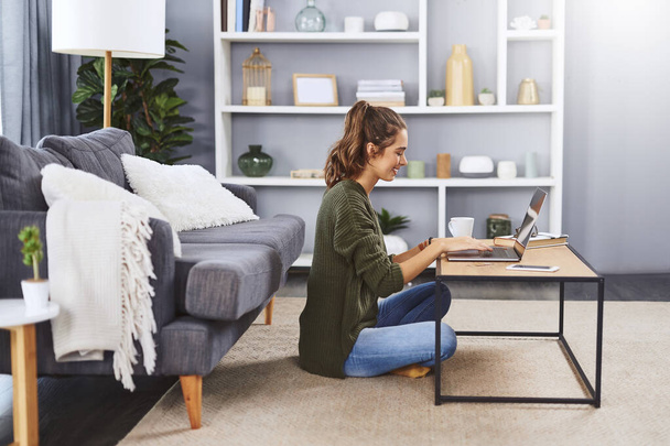 This is my comfort zone. Full length shot of a beautiful young woman sitting on the floor and using her laptop while relaxing at home - Photo, image