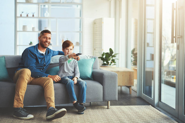 Veamos qué hay en la televisión. un niño alegre y su padre viendo la televisión juntos mientras están sentados en el sofá en casa - Foto, Imagen