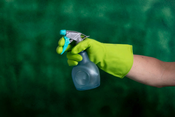 緑の背景に家の衛生のために使用される洗浄製品の保護手袋保持包装と手 - 写真・画像