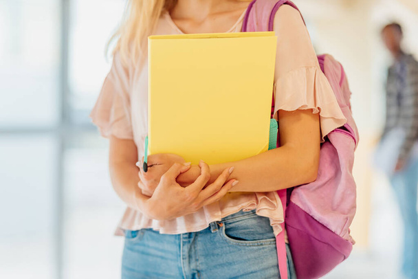 αγνώριστη νεαρή λευκή κοπέλα που κρατάει σχολικά είδη και ένα ροζ σακίδιο στις αίθουσες του γυμνασίου ή του πανεπιστημίου. Πίσω στο σχολείο. φοιτητής. - Φωτογραφία, εικόνα