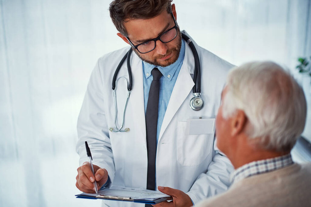Ses patients sont sa priorité. un médecin rédige des notes lorsqu'il examine un patient âgé dans une clinique - Photo, image