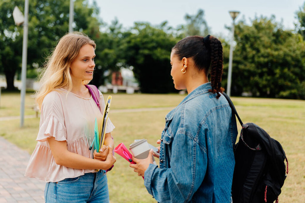 white caucasian girl with binders and backpack chatting with a latina classmate at the university campus or high school. back to school. - Photo, Image