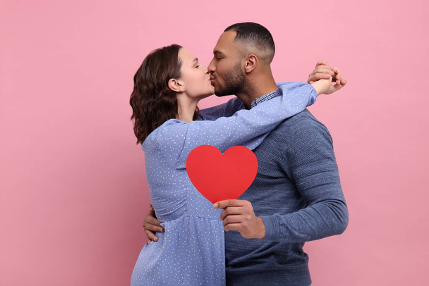 Lovely couple with red paper heart kissing on pink background. Valentine's day celebration - Zdjęcie, obraz