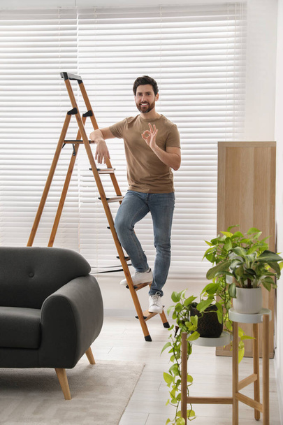 Man showing ok gesture on wooden ladder at home - Fotó, kép